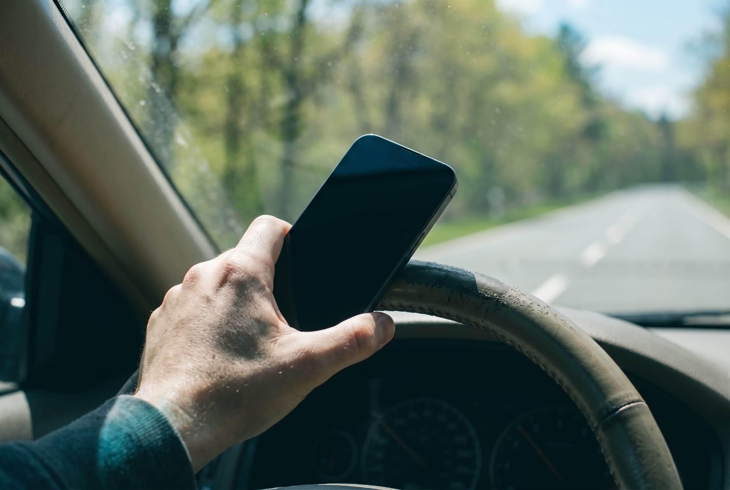 Hand mit Smartphone am Lenkrad während der Fahrt